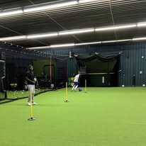 Wide shot of athlete batting in the cage with facility visible
