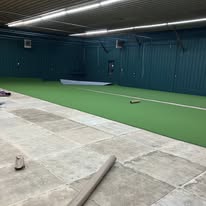 Green turf being installed on the floor with walls and lighting in place