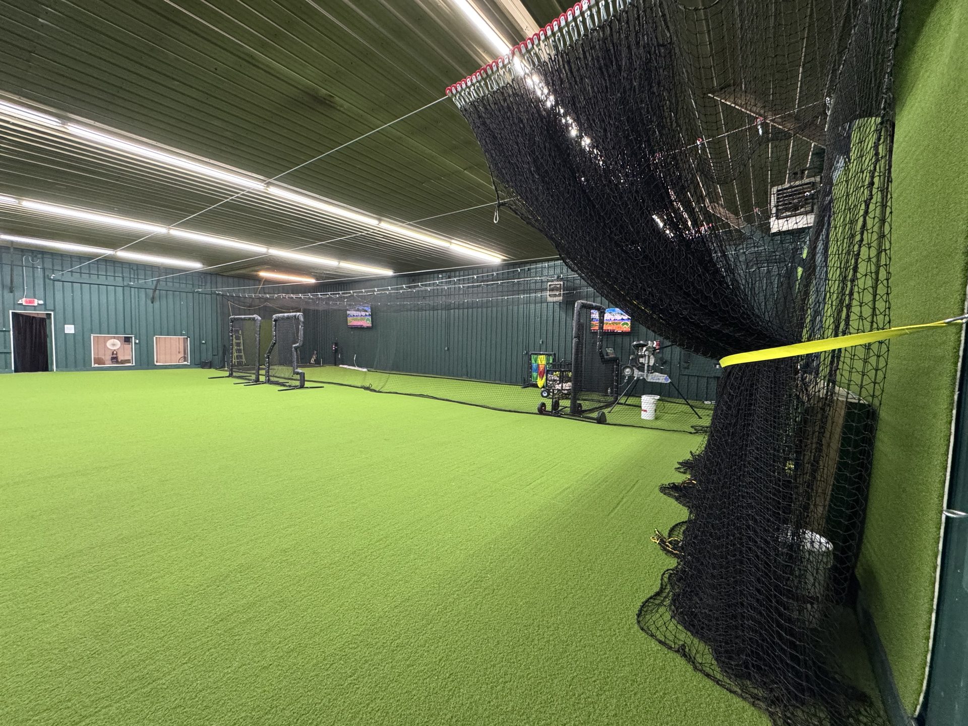 Open turf floor area with training equipment, nets, and pitching machines at Chenango SportsZone