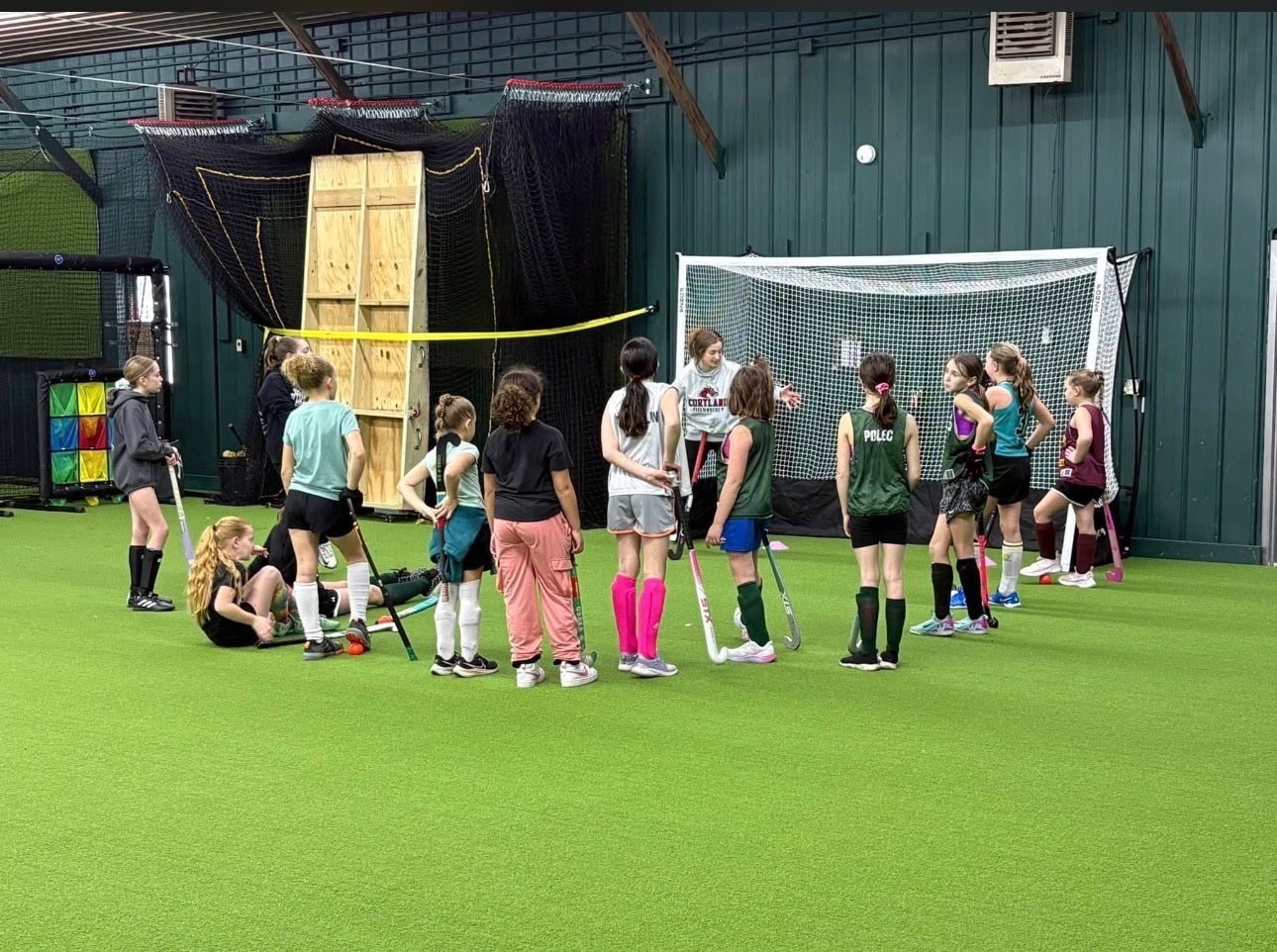 Field hockey group clinic with coach and players on the indoor turf