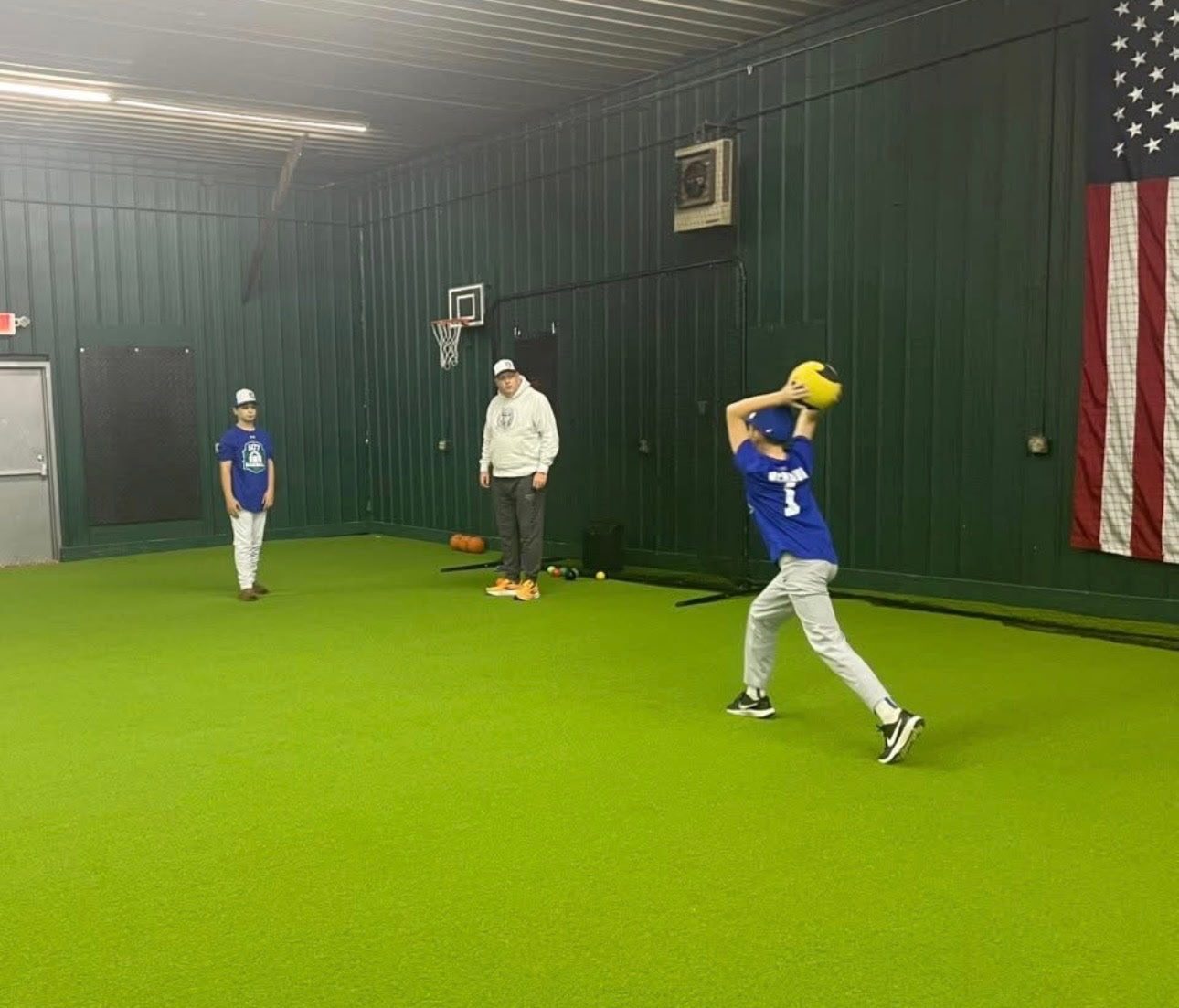 Coach working with kids in blue jerseys during a training session with American flag on the wall