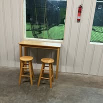 Parent viewing area with table and stools overlooking batting cages